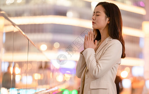 城市里双手合十祈祷的女性背景图片