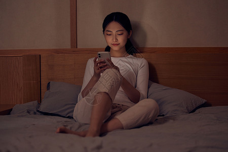 青年女性深夜睡前躺床上玩手机高清图片
