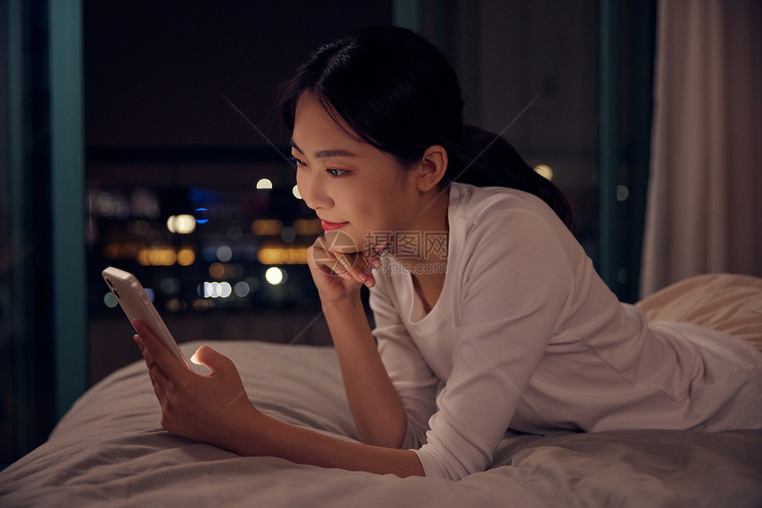青年女性深夜睡前躺床上玩手机图片