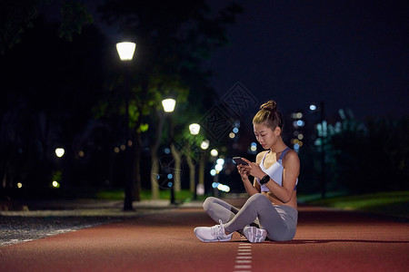 夜跑跑道城市户外夜景健身美女看手机背景