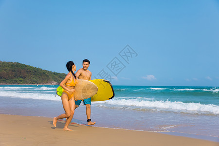 情侣拿着冲浪板奔跑在海边沙滩上图片
