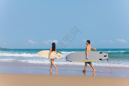 青年情侣拿着冲浪板海边沙滩上行走图片