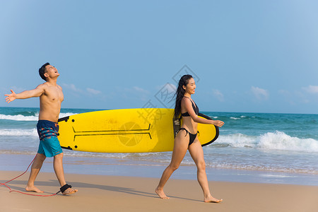 青年情侣拿着冲浪板海边沙滩上行走图片