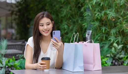美女购物消费坐在室外咖啡厅看手机背景图片