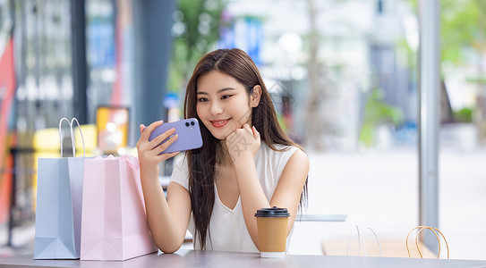 美女购物消费坐在室外咖啡厅看手机图片