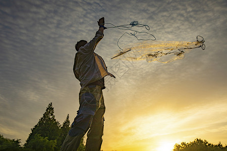 夕阳下撒网捕捞的渔民高清图片