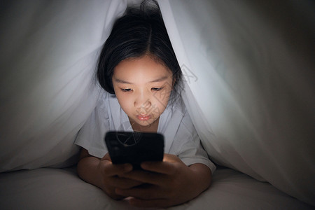 床上蜷缩素材独自在家的小女孩使用手机背景