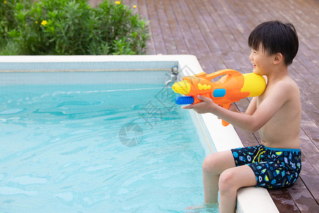 夏天游泳小孩小男孩坐在泳池边玩水枪玩具背景