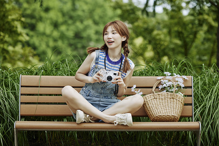 坐在长椅上拍照的夏日美女背景图片