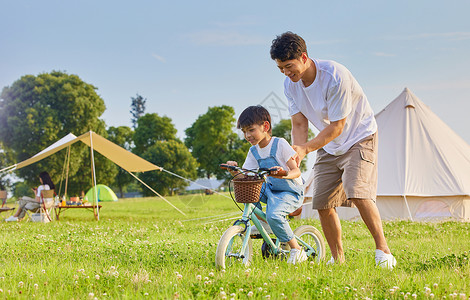 帮助小孩年轻爸爸陪伴小男孩学骑自行车背景