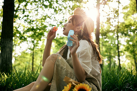 美女吹泡泡坐在草地前吹泡泡的清新夏日美女背景