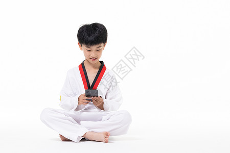 穿着跆拳道服的小男孩坐着玩手机图片