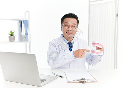 牙齿洗白中年医生手指着牙齿模型面带微笑背景