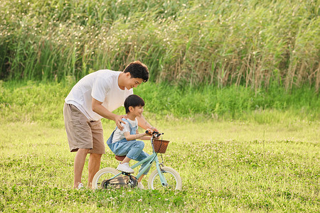 草坪小孩父子郊游爸爸教儿子骑自行车背景