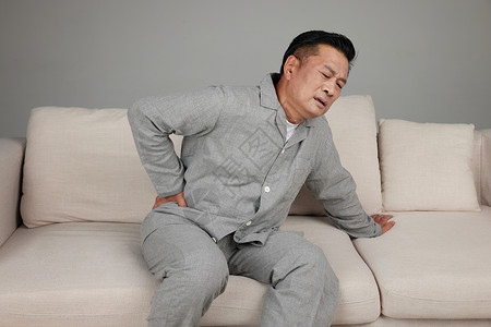45°居家中年男性坐在沙发上手扶腰部面露痛苦背景