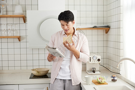 帅气的年轻男士在厨房吃早餐读报纸背景