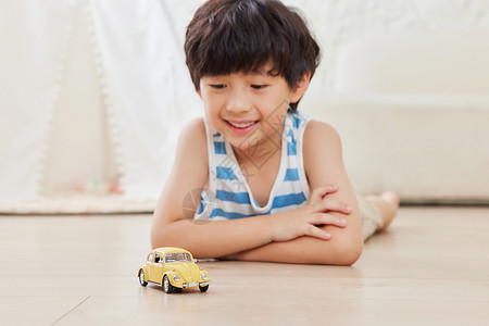黄色小汽车小男孩趴在地上看着玩具汽车背景