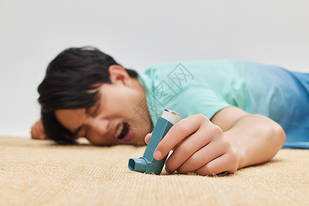 男性病患手拿哮喘吸入器男性倒在地上手拿吸入器特写背景
