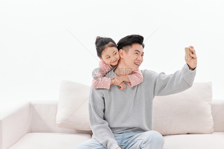 坐在沙发举起手机自拍的父女图片