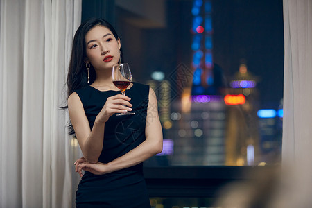 气质美女夜晚端着红酒杯站在窗前背景图片