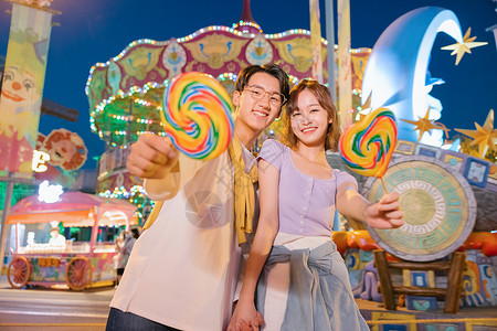 晚上情侣拿着棒棒糖的年轻情侣在游乐园玩耍背景