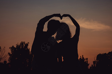 夕阳下牵手比心的情侣剪影背景图片