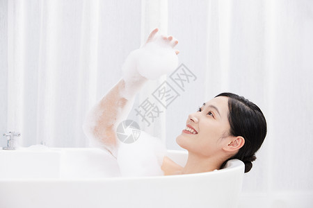 年轻女性躺在浴缸洗泡泡浴玩泡泡高清图片