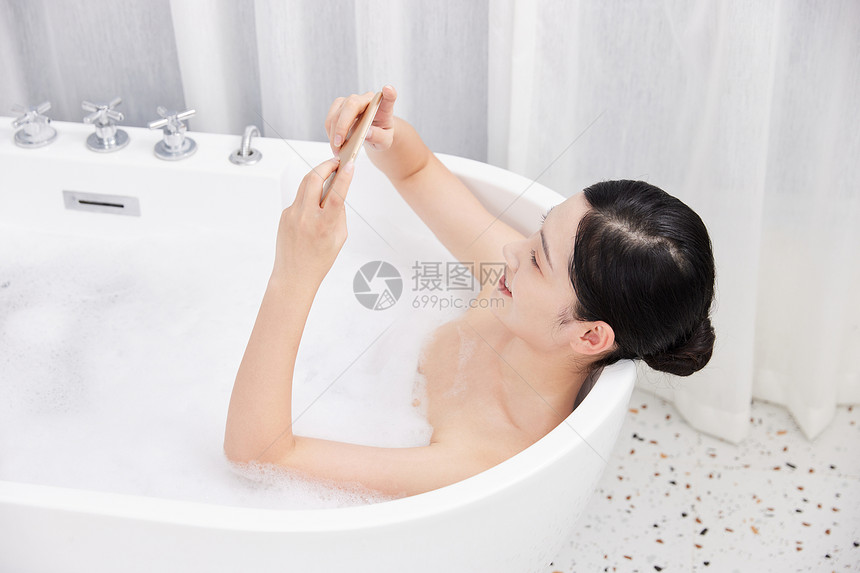 年轻女性洗泡泡浴玩手机图片