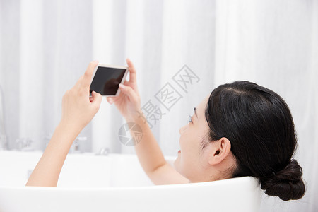 年轻女性洗泡泡浴玩手机图片