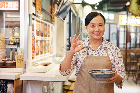 手端牛肉面的中年店员比ok手势背景图片