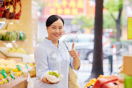 消费养老中年女性水果店内手拿葡萄点赞背景