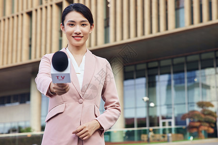 手拿话筒的青年女记者户外采访特写高清图片