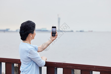 奶奶拿着手机对海边拍风景高清图片