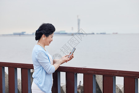 奶奶拿着手机对海边拍风景高清图片