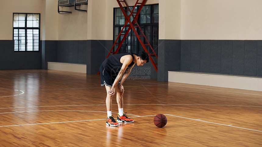 篮球运动青年手撑膝盖站在球场上图片