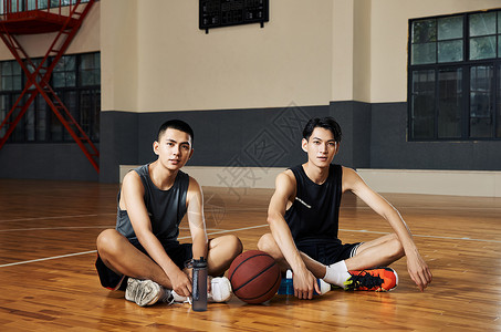 两个篮球运动青年坐在室内篮球场地板上图片
