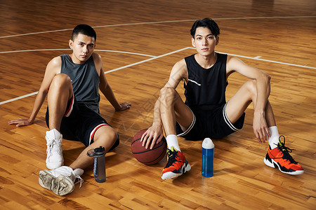 两个篮球运动青年坐在室内篮球场休息图片