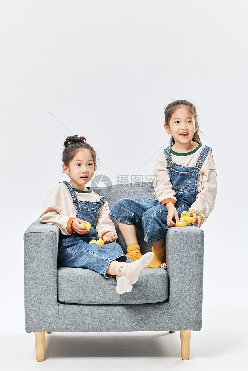 儿童双胞胎小女孩坐沙发上玩小鸭子玩具图片