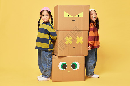 双胞胎小女孩躲在创意纸盒箱旁边背景图片