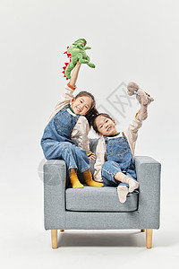 绒毛沙发儿童双胞胎小女孩坐沙发上玩绒毛玩偶背景