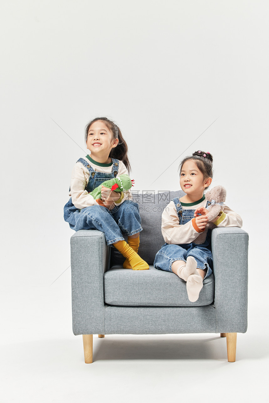 双胞胎小女孩坐沙发上玩绒毛玩具图片