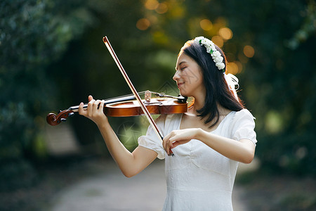 逆光森林夕阳余晖中拉小提琴的少女背景