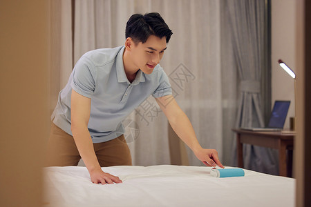 年轻男士使用粘毛器滚刷床单图片