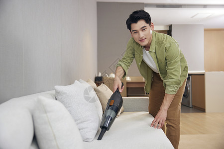 年轻男青年使用吸尘器给沙发除尘背景图片