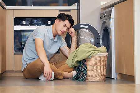 年轻男性居家洗衣服年轻男性看着脏衣服苦恼背景