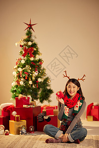 幸福圣诞节美女圣诞节手拿礼物坐在圣诞树和礼物前背景