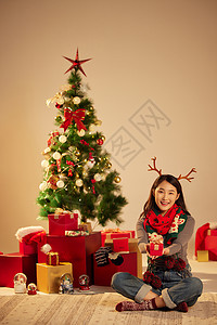 美女圣诞节手拿礼物坐在圣诞树和礼物前高清图片