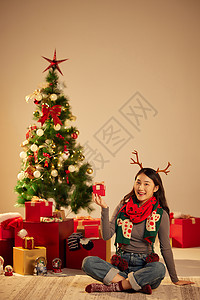 美女圣诞节手拿礼物坐在圣诞树和礼物前图片