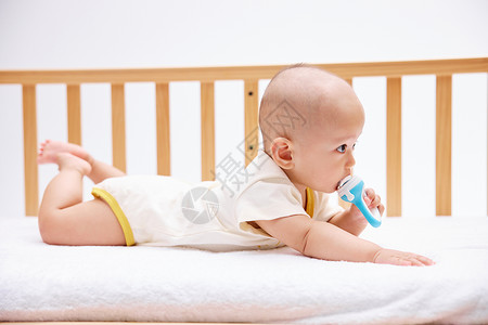 吃奶嘴的可爱宝宝在婴儿床里玩耍图片