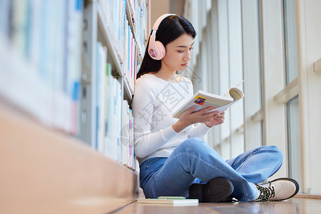 人听歌女学生在图书馆看书听音乐背景